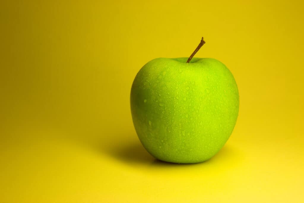 Wet green apple on yellow background